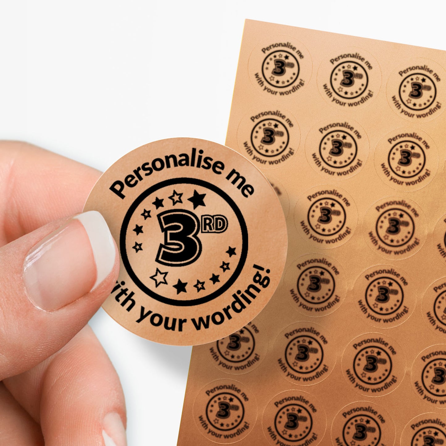 Sheet of circular stickers with 3rd in the middle and text on a bronze background. Single sticker held between thumb and finger