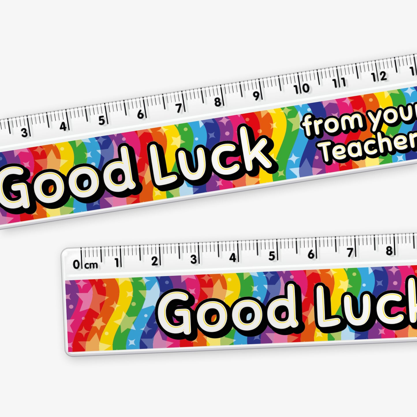 Close up of a 15cm ruler featuring a vibrant rainbow background with stars and bold yellow and white text reading 'Good Luck from your Teacher' along the centre.