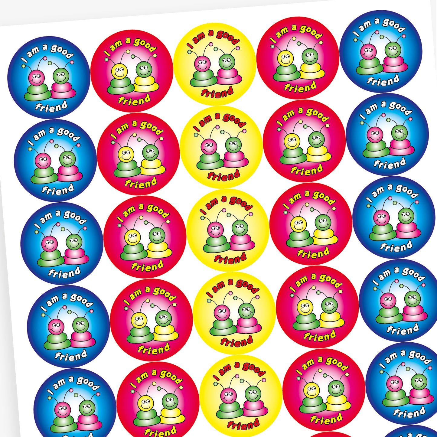 A sheet of round reward stickers in various bright colours, each with the phrase 'I am a good friend' written in bold, playful text. Each sticker features two cartoon alien-like characters with antennae, sitting side by side and smiling. The background colours include red, blue, yellow, and pink gradients, creating a cheerful and encouraging design aimed at promoting positive social behaviour.