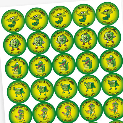 A sheet of round motivational stickers with a green and yellow gradient background. Each sticker features the phrase 'I've been GREEN all week!' in playful black text. The centre of each sticker displays a different cheerful green character: a worm with glasses, a shiny star, a friendly dinosaur, and a smiling apple. These stickers are designed to reward consistent positive behaviour over the week.