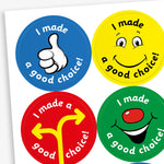 A sheet of four colourful circular reward stickers for children, each with the phrase 'I made a good choice!'. Top left: a blue background with a thumbs-up illustration. Top right: a yellow background with a smiling cartoon face. Bottom left: a red background with a yellow direction sign. Bottom right: a green background with a smiling face featuring a red nose.