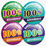 Four colourful circular badges each stating 'Autumn Term 100% Attendance' in bold text. The badges are in blue and cyan, cyan and blue, green and purple, and purple with orange. Designed to reward full attendance during the autumn school term.