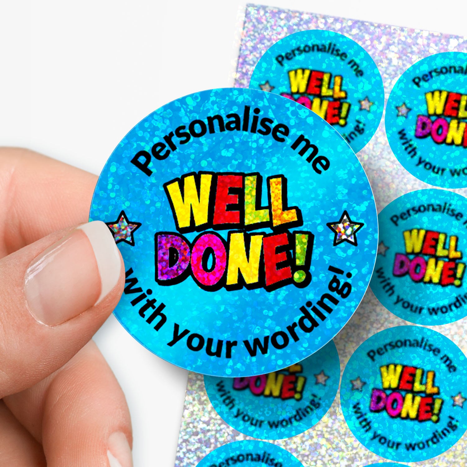 Blue sticker with 'Well Done!' text on a glittery background held by a hand with a sheet of stickers in the background.