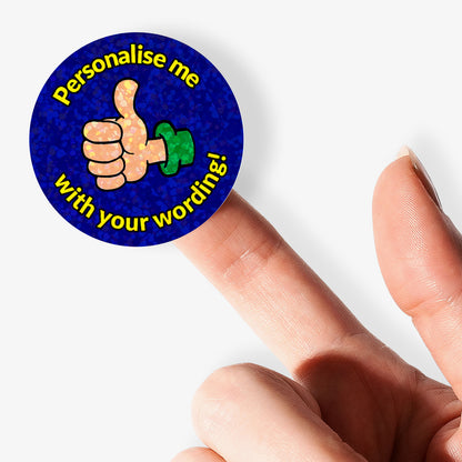 Round sticker with a thumbs-up icon and text 'Personalise me with your wording!' held between fingers.