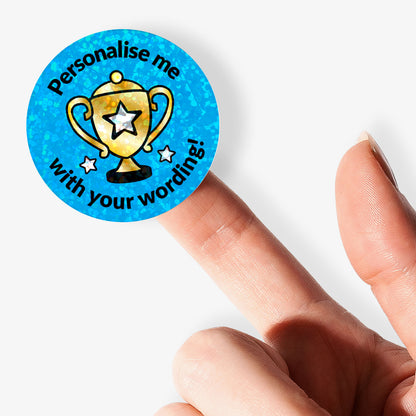 Personalised holographic round sticker with trophy design and text 'Personalise me with your wording' held with finger.
