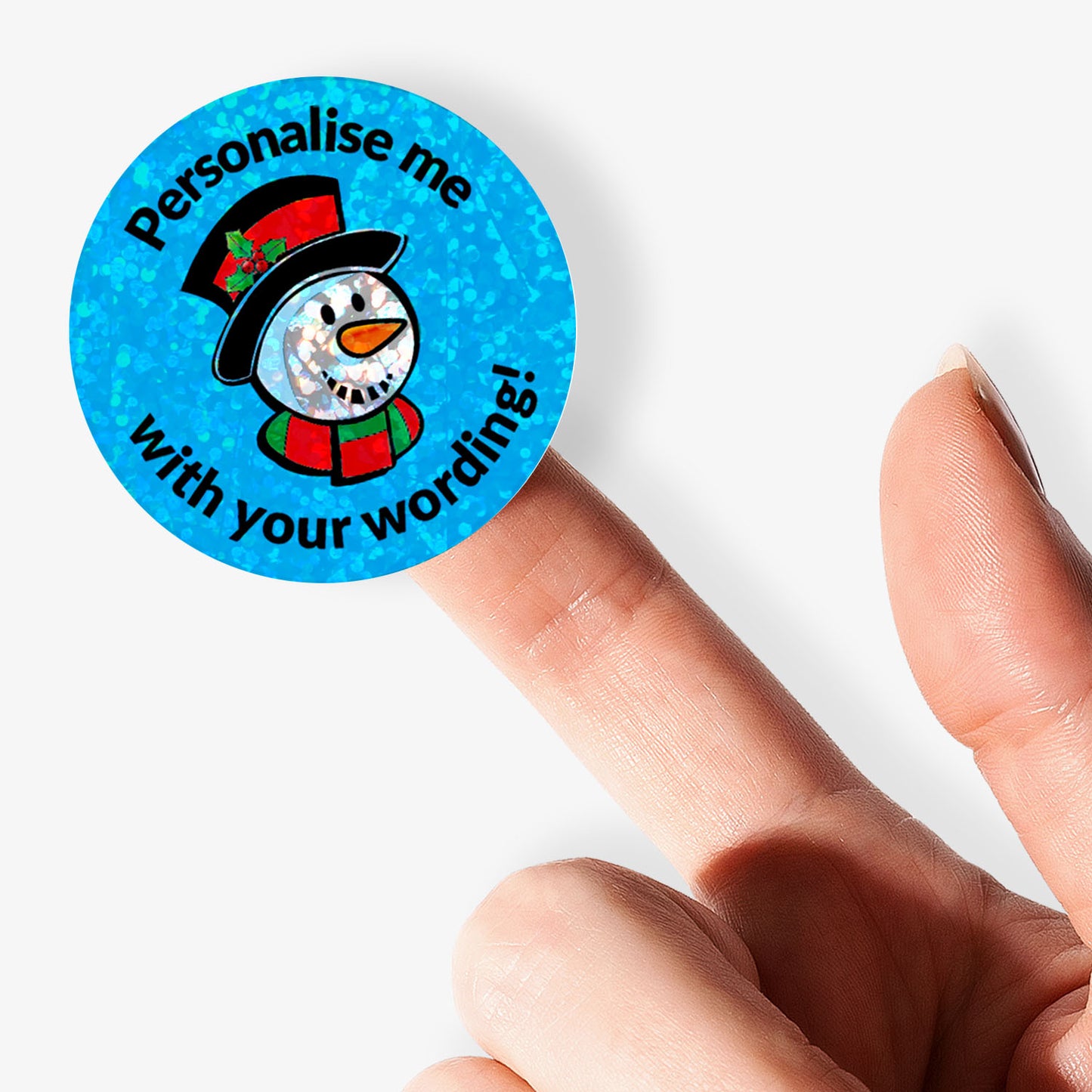 Round blue sticker with snowman graphic and text 'Personalise me with your wording!' held between fingers.