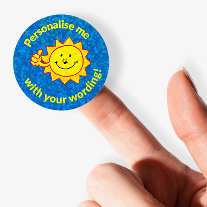 Round sticker with sun design and text 'Personalise me with your wording!' held between fingers.