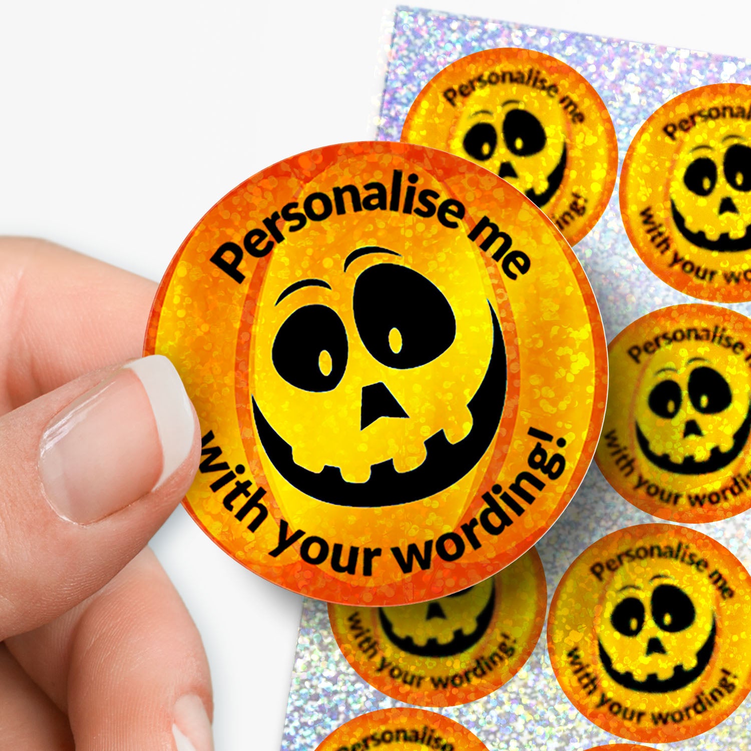 Circular sticker with sparkly pumpkin design and personalised text held by a hand with sheet of stickers in the background.