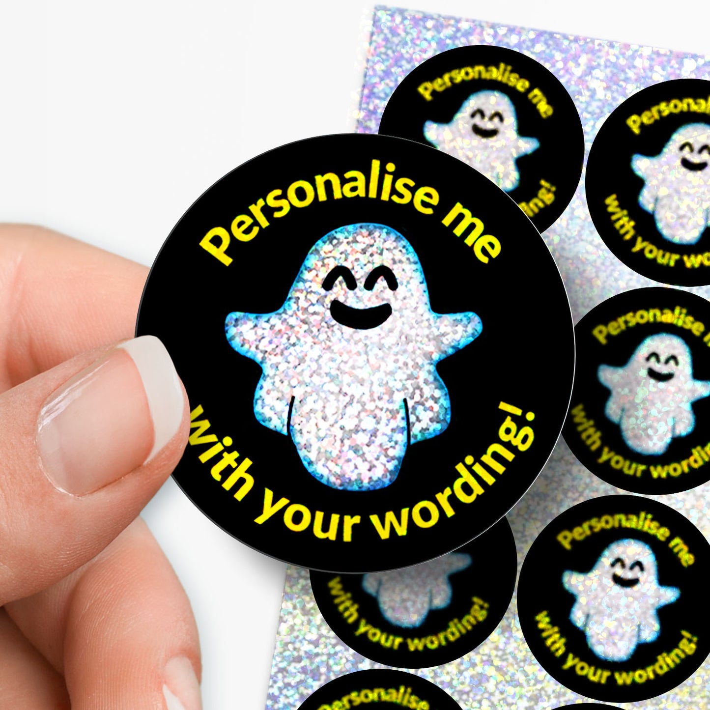 Circular sticker with sparkly spooky ghost design and personalised text held by hand with sticker sheet in the background.