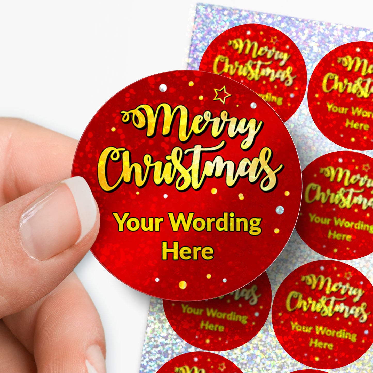 Red round Christmas sticker with 'Merry Christmas Your Wording Here' text, held by a hand with sheet in the background.