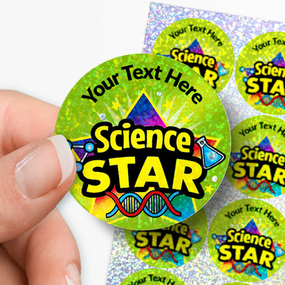 Sparkly colorful 'Science STAR' sticker with customisable text held by hand with sheet of stickers in the background.