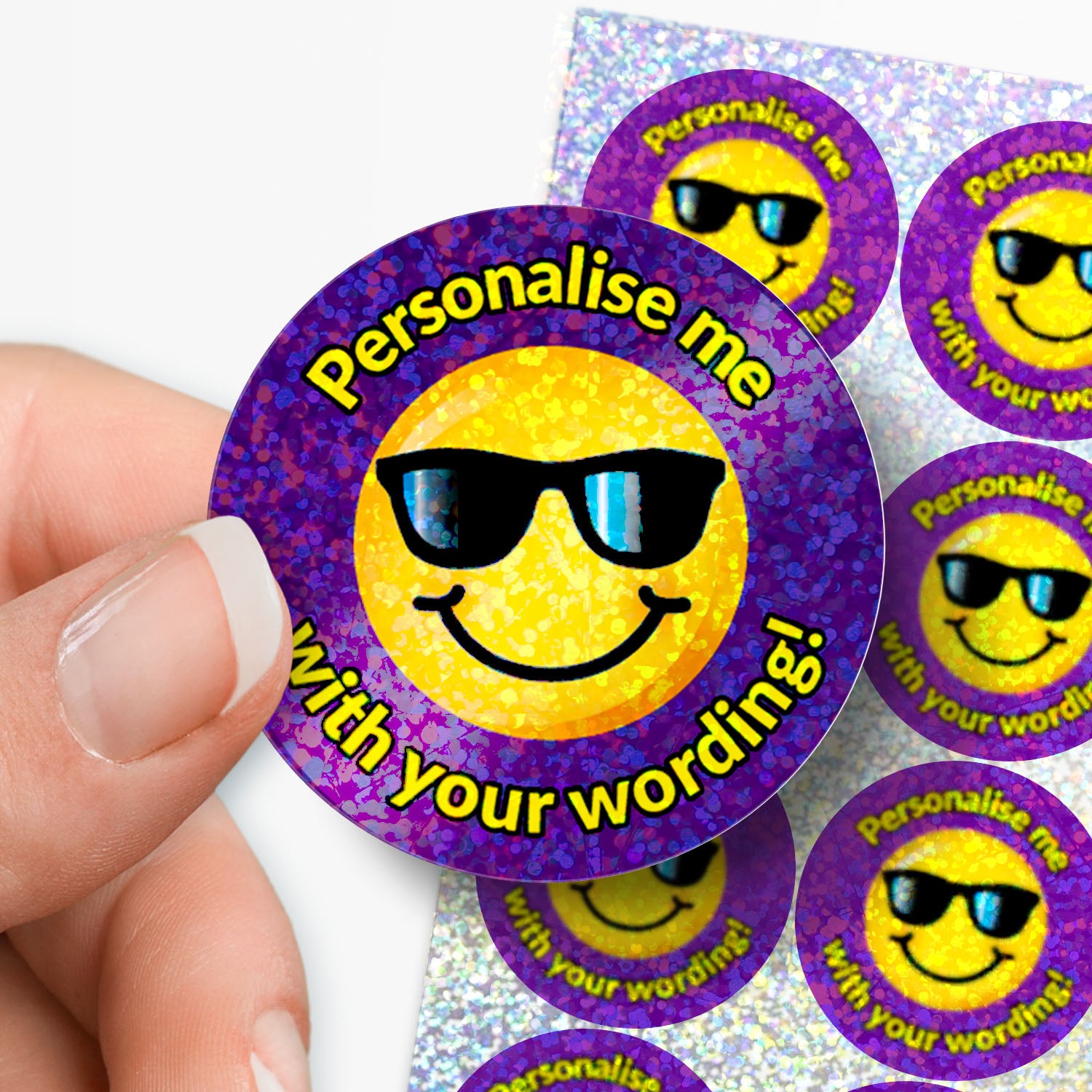Smiley face with sunglasses stickers with 'Personalise me with your wording!' text, held by a hand with a sheet of stickers in the background.