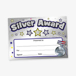 A5-sized holographic silver award certificate featuring a bold 'Silver Award' title with a glittery effect, a silver medal illustration in the bottom right corner and star emblems. Designated spaces for recipient's name, reason for the award, signature, and date.
