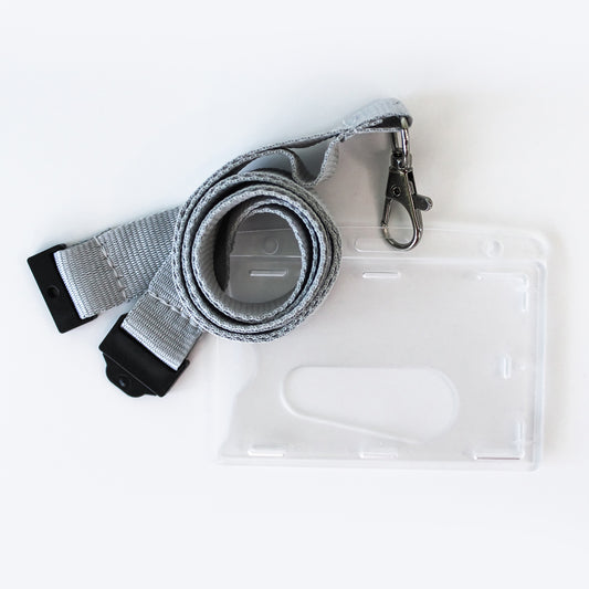 A grey woven lanyard with black plastic quick-release buckles and a silver metal clasp, shown next to a clear plastic ID badge holder on a white background.