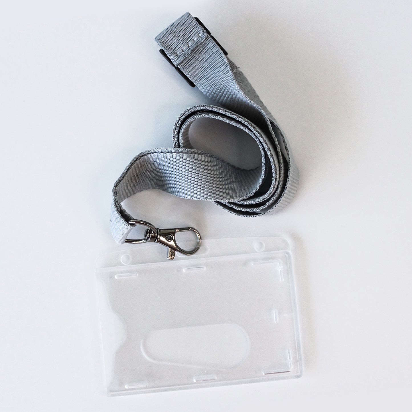 A grey woven lanyard with a silver metal clasp attached to a clear plastic ID badge holder, photographed on a plain white background.