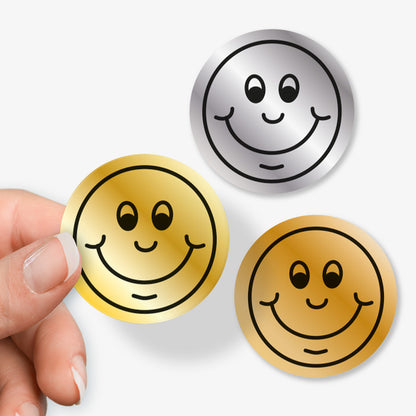 Three smiley face buttons in gold, silver, and bronze held by a hand on a white background.