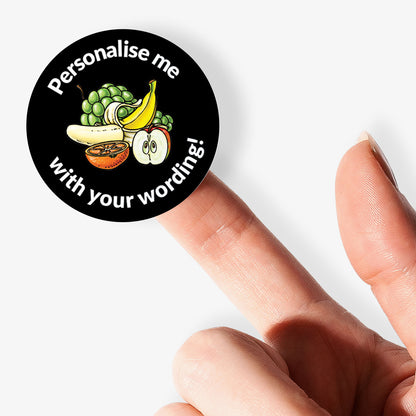 Round customizable sticker with fruit illustrations and text on a finger
