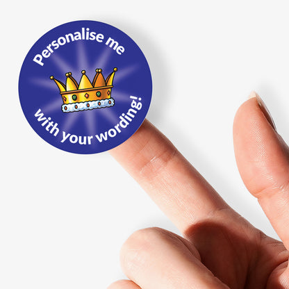 Round customizable badge with a crown design held by a finger on a white background