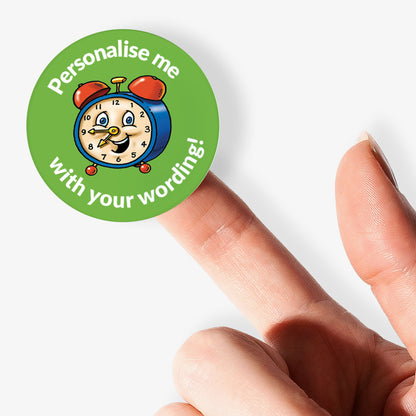 Circular sticker with a cartoon clock and text 'Personalise me with your wording!' held by a finger.