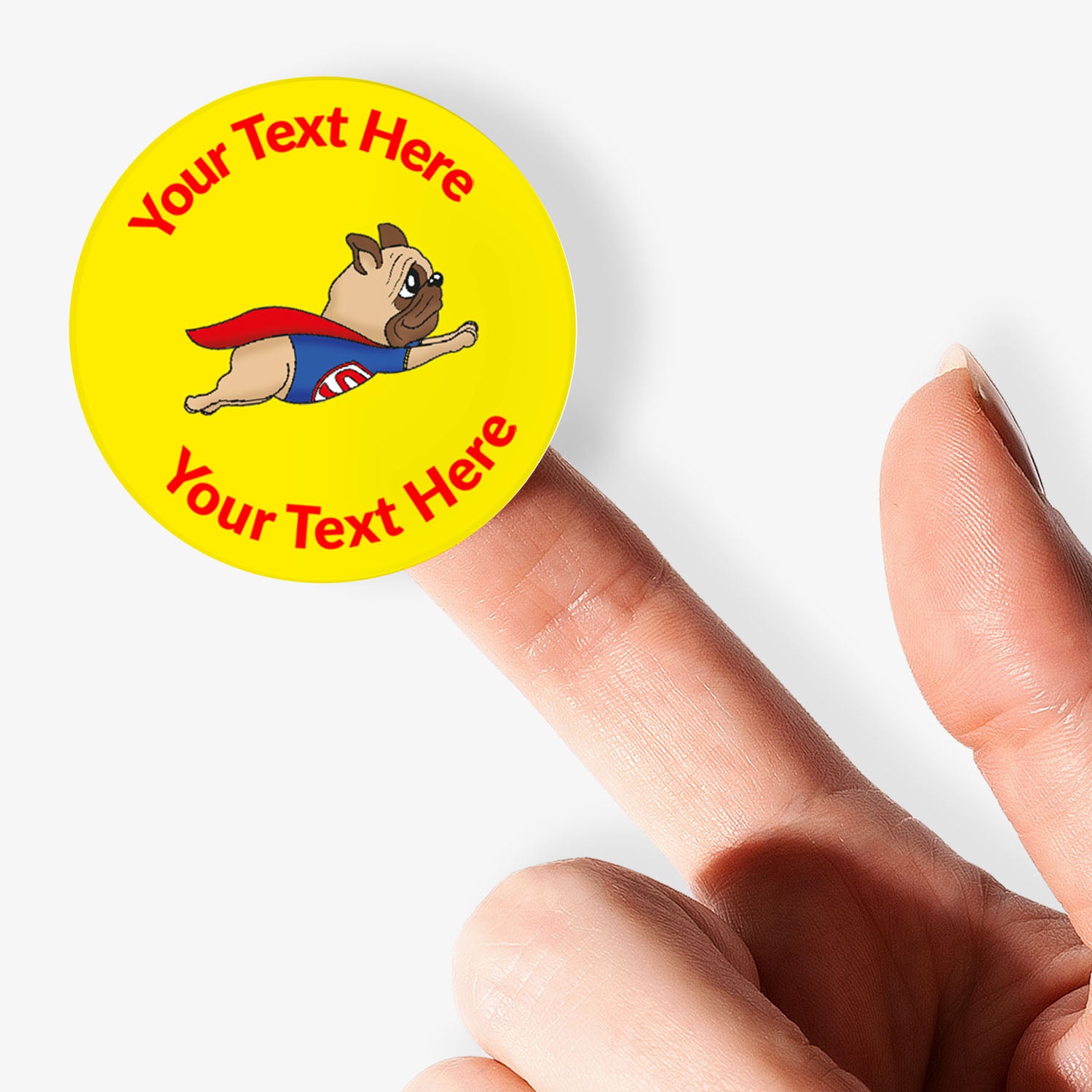 Round yellow sticker with superhero dog graphic and customizable text held between fingers.