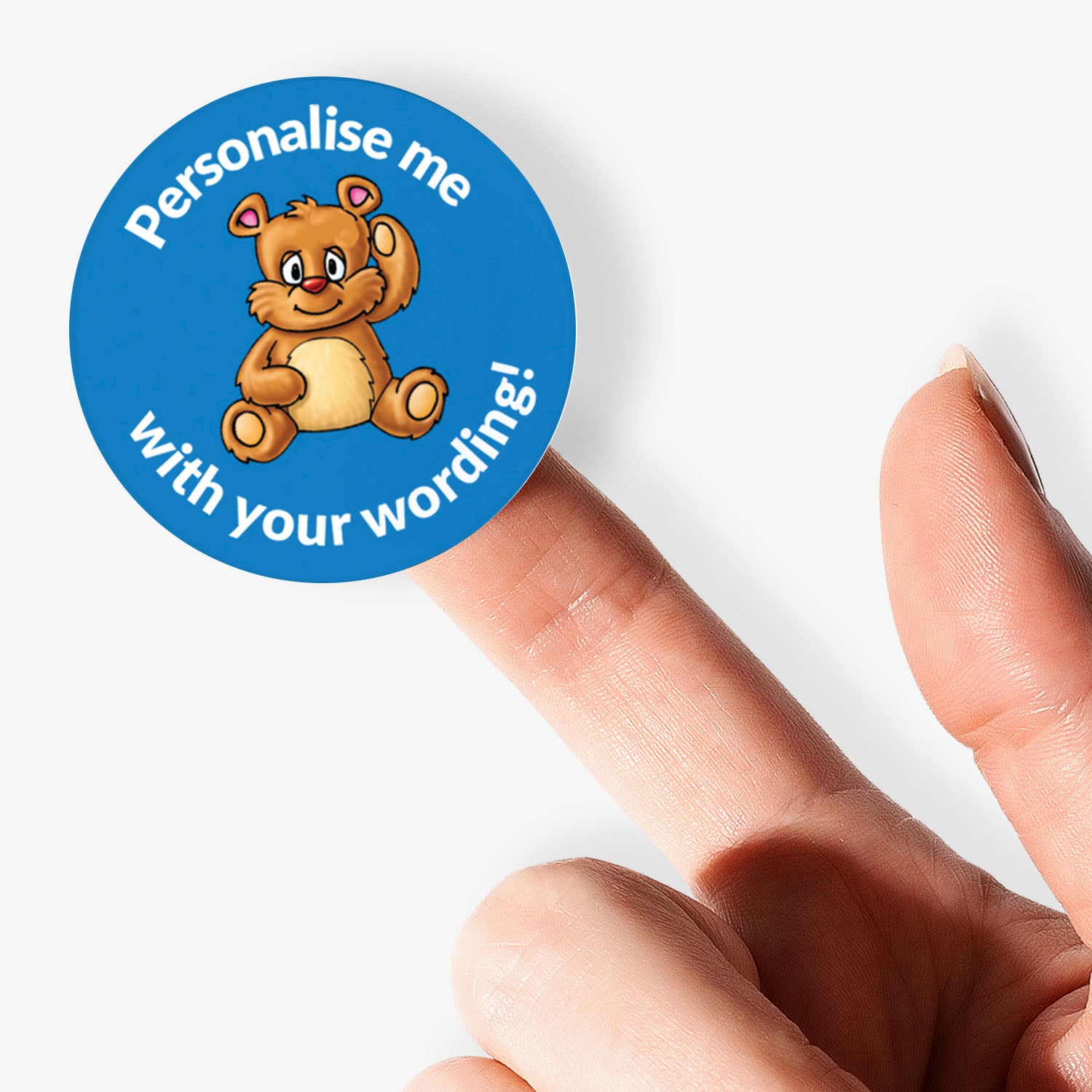 Round sticker with teddy bear graphic and text 'Personalise me with your wording!' held by a finger.