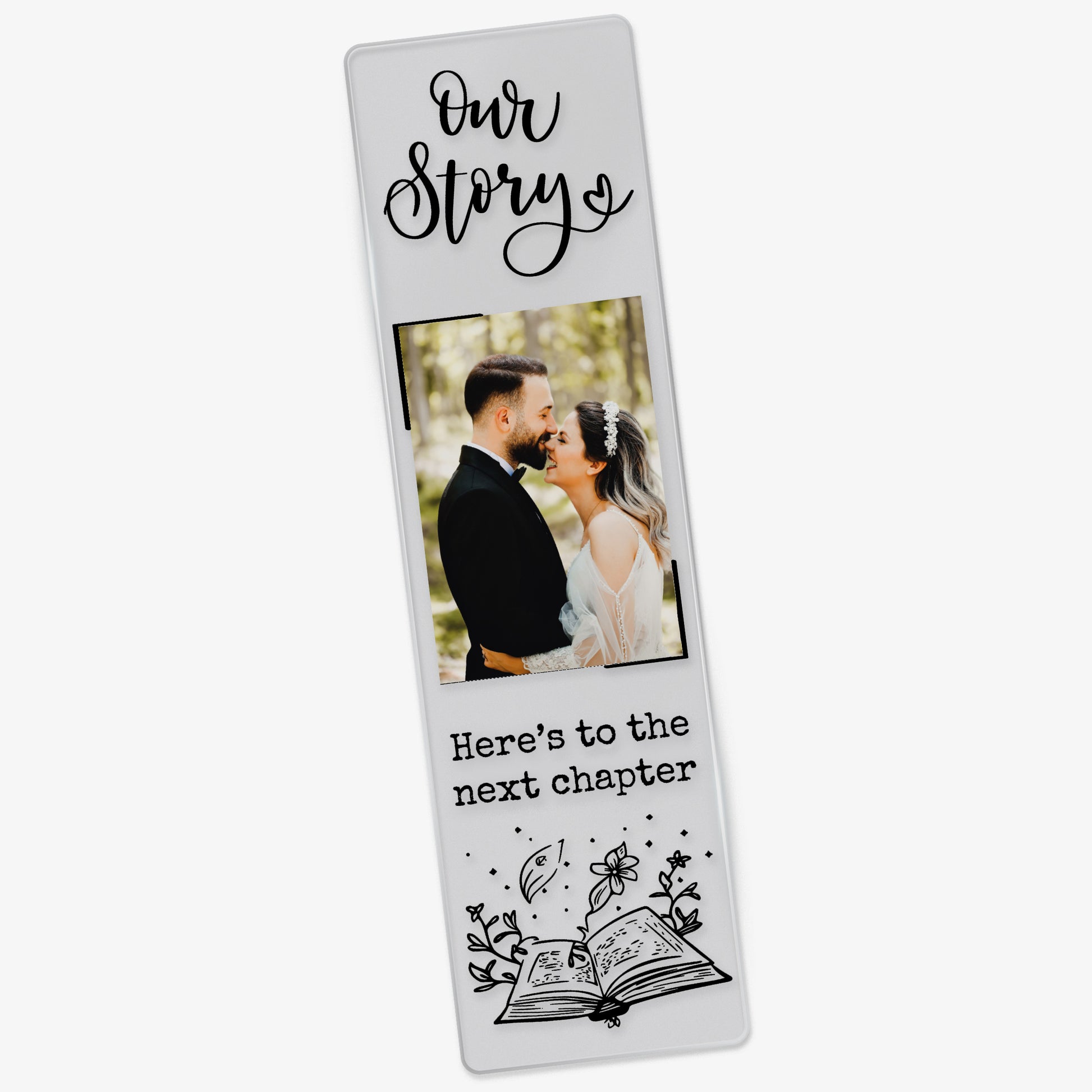 Clear acrylic wedding-themed bookmark featuring the phrase 'Our Story' at the top, a photo of a couple in wedding attire, and the words 'Here’s to the next chapter' in black font above an illustrated open book with magical elements.