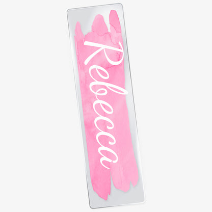 Acrylic bookmark with a pale pink watercolour brush stroke vertically down the middle with white script font 'Rebecca'.