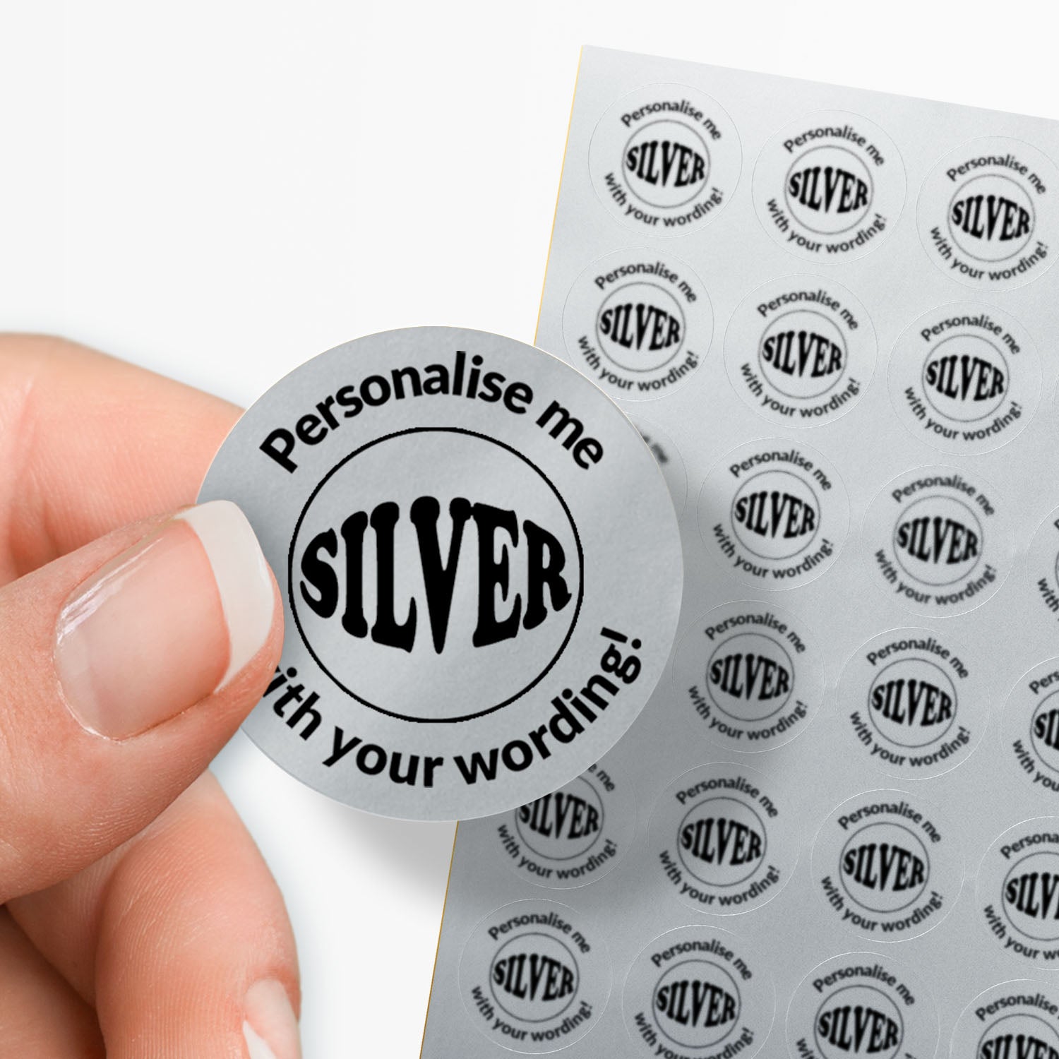 Round silver sticker with 'Personalise me SILVER with your wording!' text held by a hand, with a sheet of similar stickers in the background.