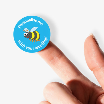 Blue sticker on a finger with a bee as a central image.  'Personalise me with your wording!' surrounds the image.