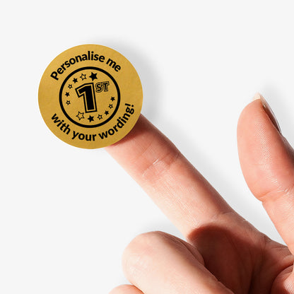 Gold sticker with text 'Personalise me 1st with your wording!' held between fingers on a white background