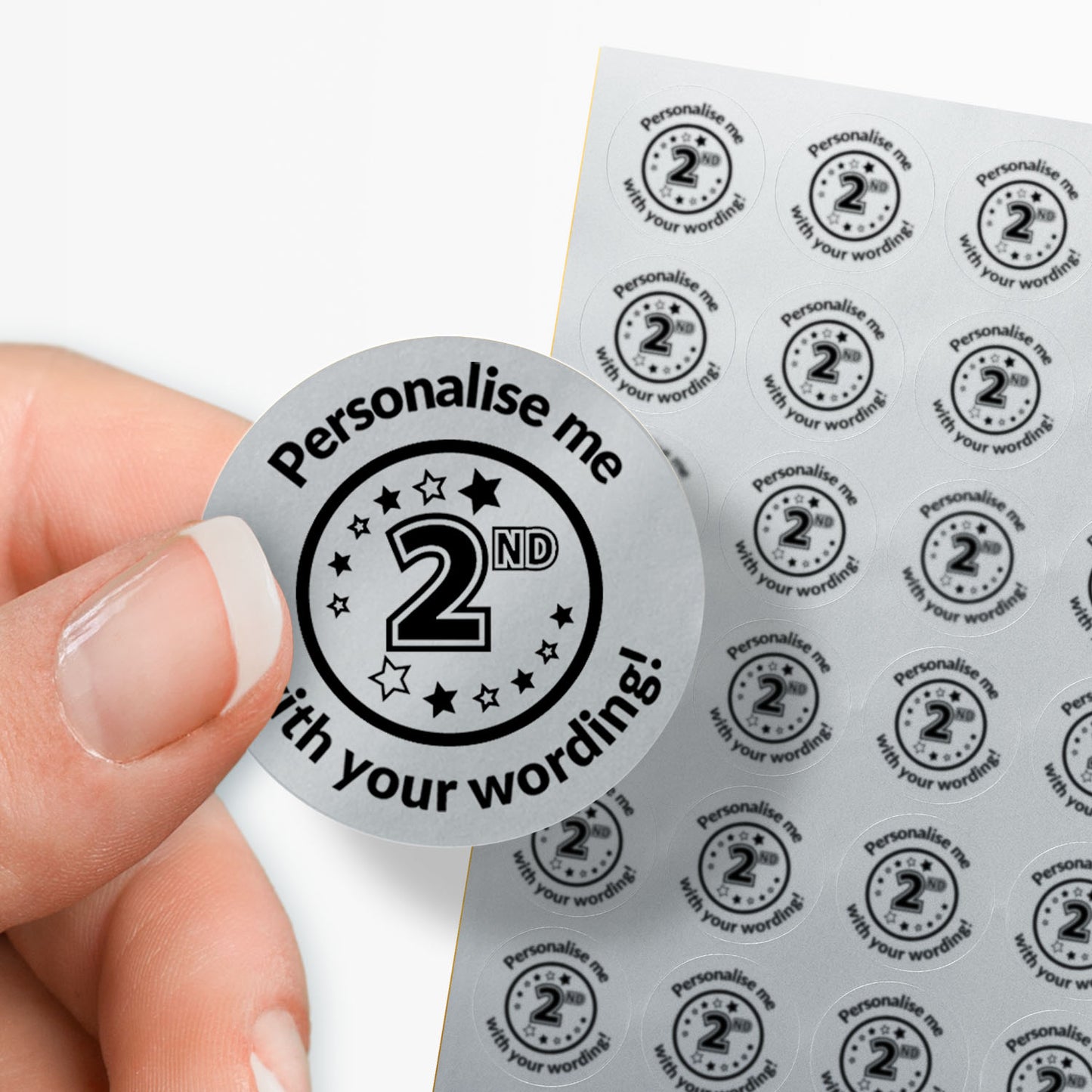 Sheet of circular stickers with 2nd in the middle and text on a silver background. Single sticker held between thumb and finger