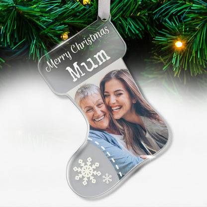 Stocking-shaped acrylic Christmas tree ornament with a cleardesign, white snowflake decorations, and the message in white font 'Merry Christmas Mum' at the top, featuring a photo of two smiling women, one older and one younger, hugging each other, hanging on a tree with fairy lights.