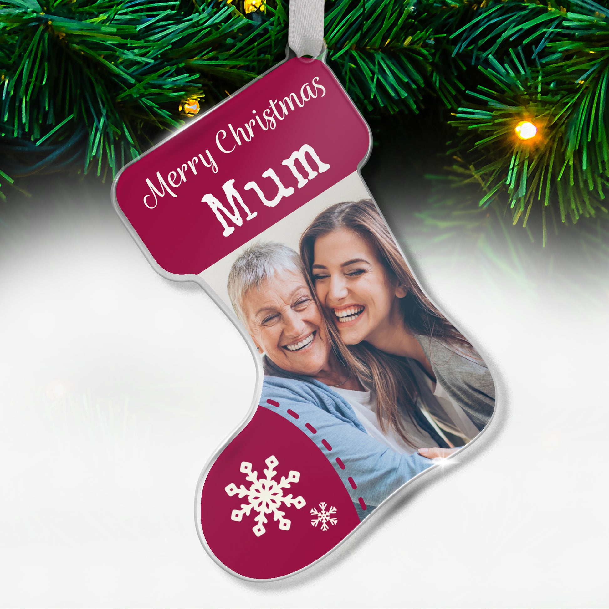Stocking-shaped acrylic Christmas tree ornament with a maroon design, white snowflake decorations, and the message 'Merry Christmas Mum' at the top, featuring a photo of two smiling women, one older and one younger, hugging each other, hanging on a tree with fairy lights.