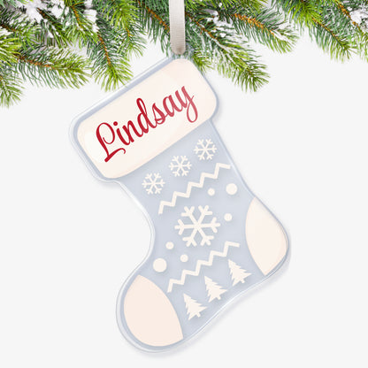Clear acrylic Christmas stocking-shaped tree ornament decorated with a snow scene with 3 christmas trees and snowflakes in white; The heel, toe and top are white featuring a space at the top for a customisation saying 'Lindsay' in redscript, hanging on a Christmas tree.