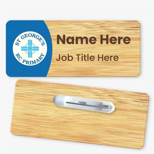 Front and back view of a rectangular bamboo name badge. The front displays the St George's RC Primary School logo on a blue panel, with placeholder text for 'Name Here' and 'Job Title Here'. The back features a metal safety pin fastening for attachment.