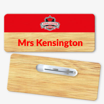 A rectangular bamboo name badge with a natural background and a red top section. The text reads 'Mrs Kensington' in bold red letters on the natural part, and there is a school logo placed centrally on the top red section. The reverse side of the badge is also shown, featuring a metal safety pin fastening for attachment.