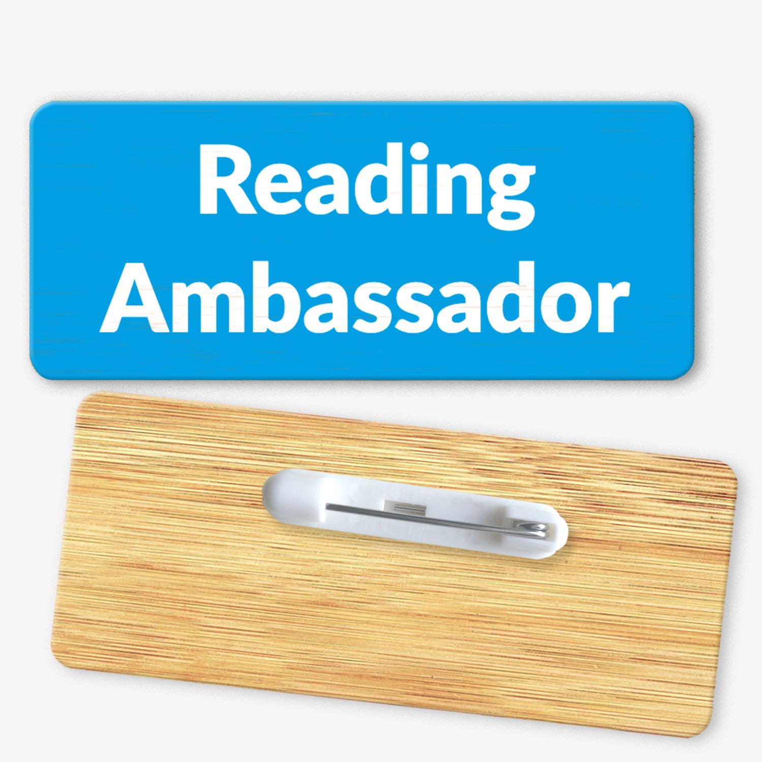 A rectangular bamboo name badge with a cyan background. The text reads 'Reading Ambassador' in bold white letters. The reverse side of the badge is also shown, featuring a metal safety pin fastening for attachment.