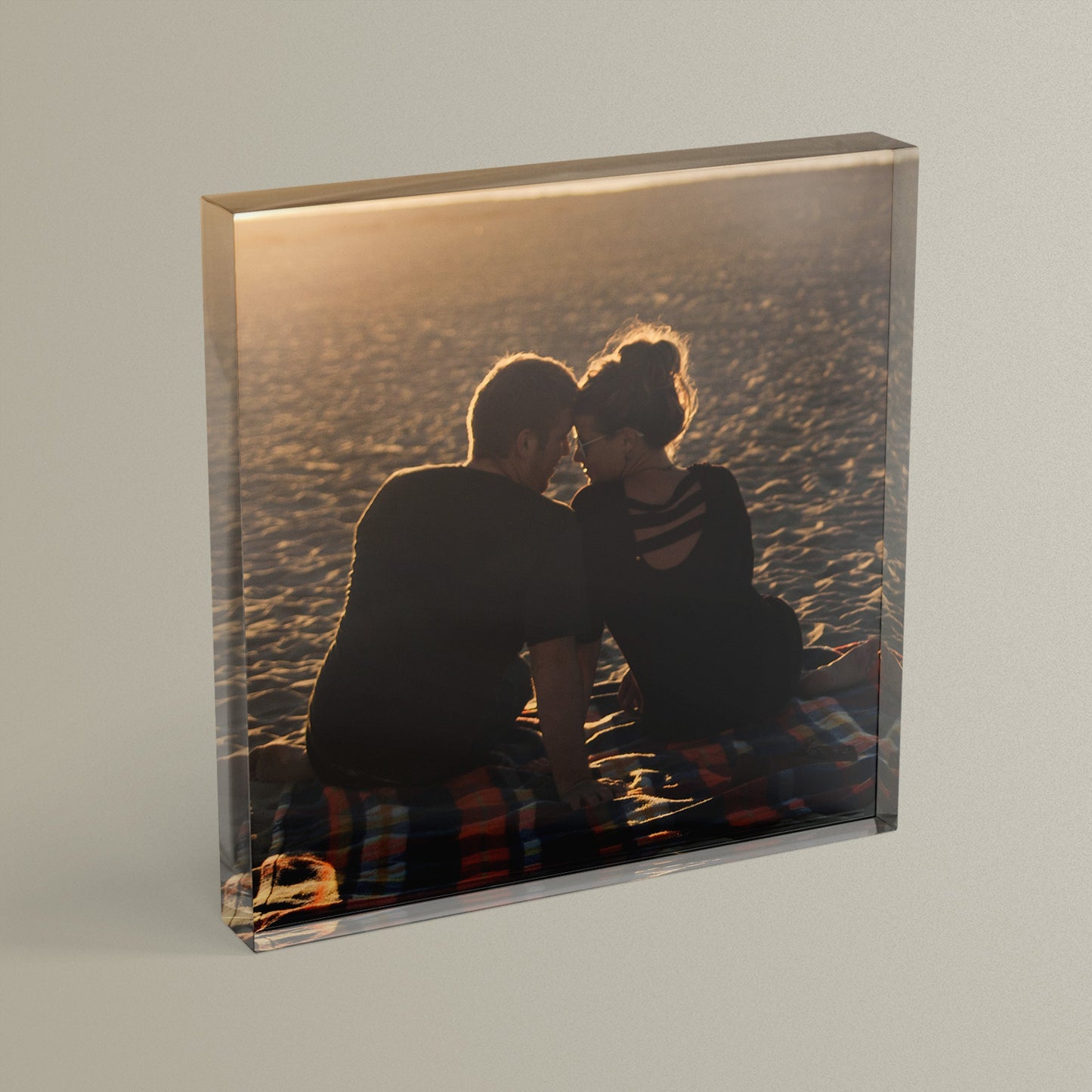 A square acrylic photo block featuring a photo of a couple on a blanket on a beach.  The block has a glossy, freestanding design ideal for display.