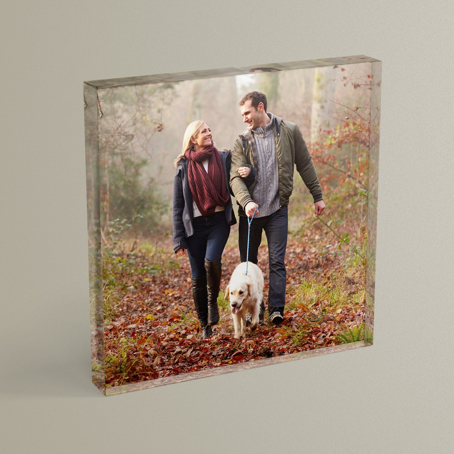 A square acrylic photo block featuring a photo of a couple walking a dog in the woods.  The block has a glossy, freestanding design ideal for display.