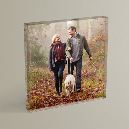 A square acrylic photo block featuring a photo of a couple walking a dog in the woods.  The block has a glossy, freestanding design ideal for display.