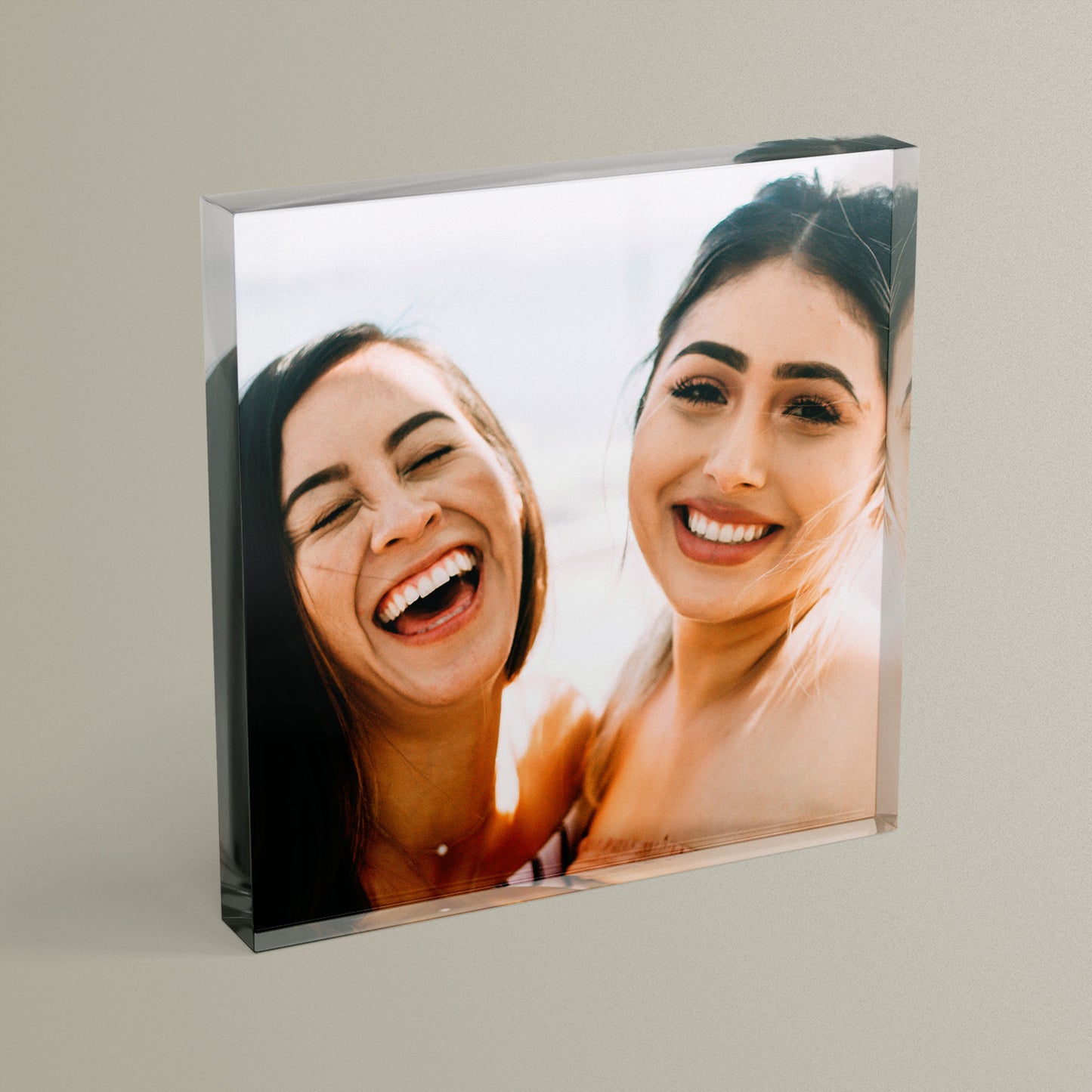 A square acrylic photo block featuring a photo of two friends laughing.  The block has a glossy, freestanding design ideal for display.