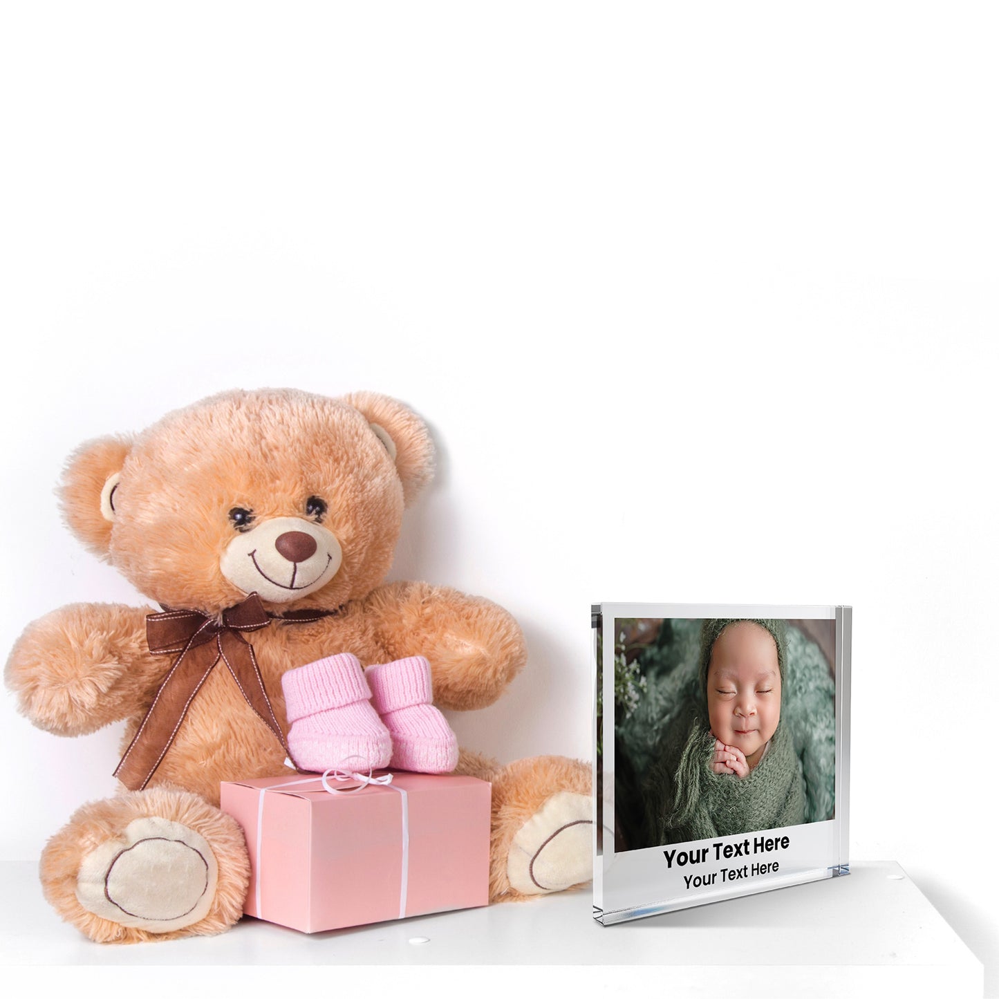 A square acrylic photo block featuring a baby photo. The image shows a new born baby. Beneath the photo, printed placeholder text reads 'Your Text Here' followed by  'Your Text Here'. The block has a glossy, freestanding design ideal for display.  The photo block is positioned next to a teddy bear.
