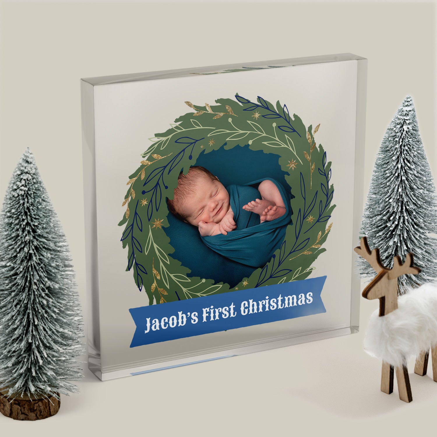 Acrylic block with a photo of a baby in a wreath with 'Jacob's First Christmas' text, surrounded by decorative trees and a deer.