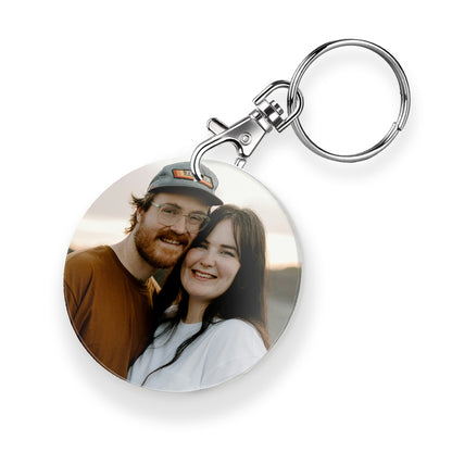 A personalised keyring featuring a circular photo frame design with a metal keychain and clasp. The photo shows a couple together.