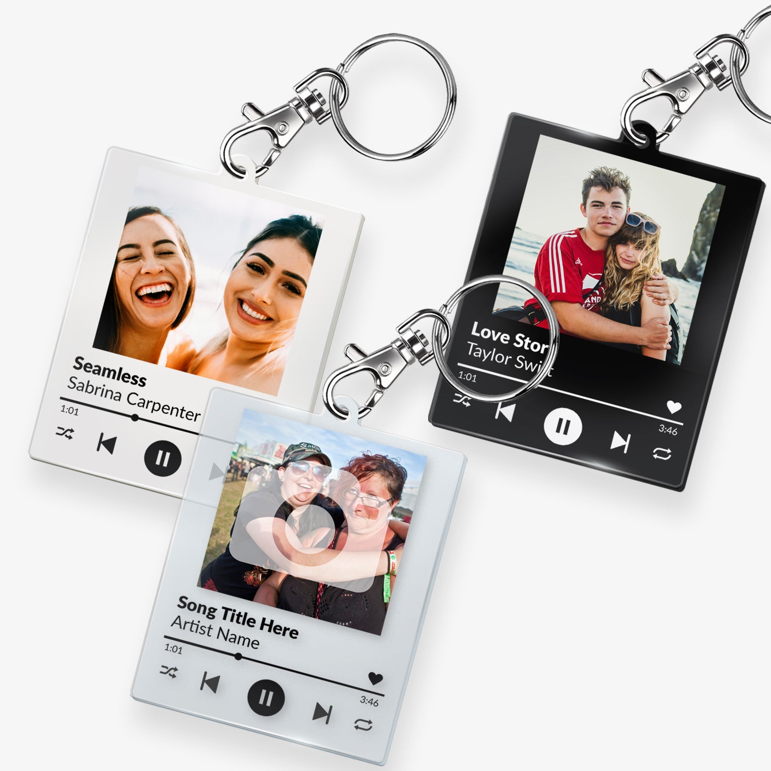 A custom acrylic keyring designed to resemble a digital music player interface. It features a square frame with a photo of two smiling people at the top. Below the photo are mock song details, including placeholder text 'Song Title Here' and 'Artist Name'. Music control icons—rewind, play, forward, and a heart—are displayed along the bottom, mimicking a streaming app. The keyring is attached to a metal clasp and keyring loop.