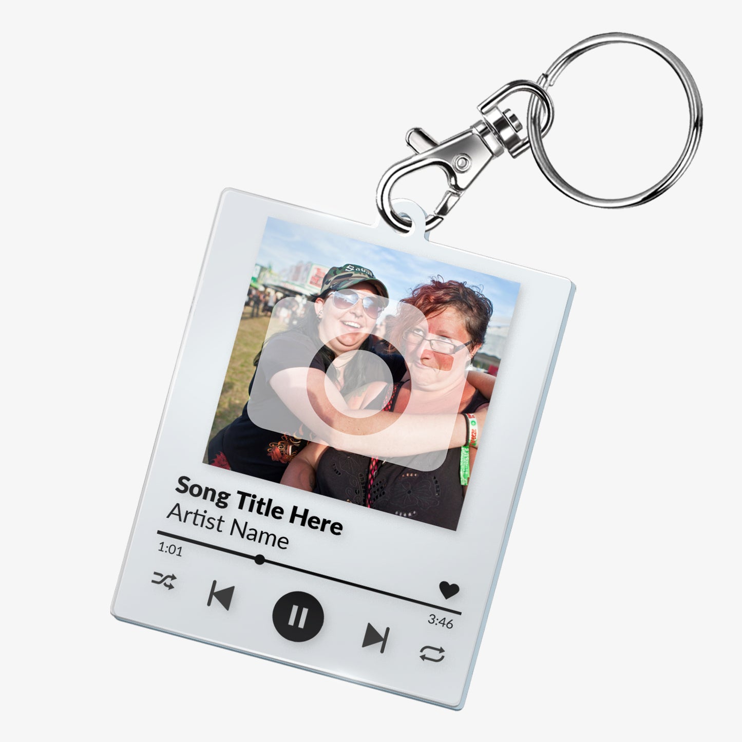 A custom acrylic keyring designed to resemble a digital music player interface. It features a square frame with a photo of two smiling people at the top. Below the photo are mock song details, including placeholder text 'Song Title Here' and 'Artist Name'. Music control icons—rewind, play, forward, and a heart—are displayed along the bottom, mimicking a streaming app. The keyring is attached to a metal clasp and keyring loop.