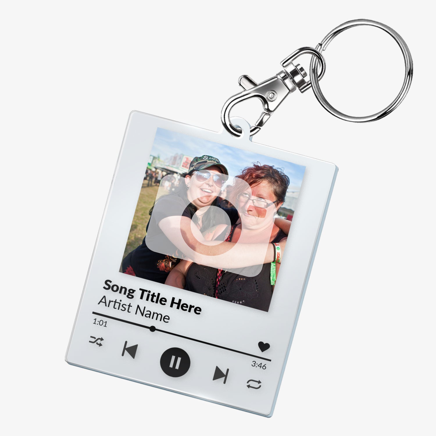 A custom acrylic keyring designed to resemble a digital music player interface. It features a square frame with a photo of two smiling people at the top. Below the photo are mock song details, including placeholder text 'Song Title Here' and 'Artist Name'. Music control icons—rewind, play, forward, and a heart—are displayed along the bottom, mimicking a streaming app. The keyring is attached to a metal clasp and keyring loop.