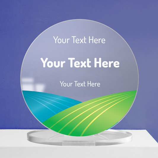 Round acrylic award plaque on a clear base, featuring a stylised green and blue landscape graphic at the bottom and three lines of placeholder text for custom wording, displayed against a blue background.