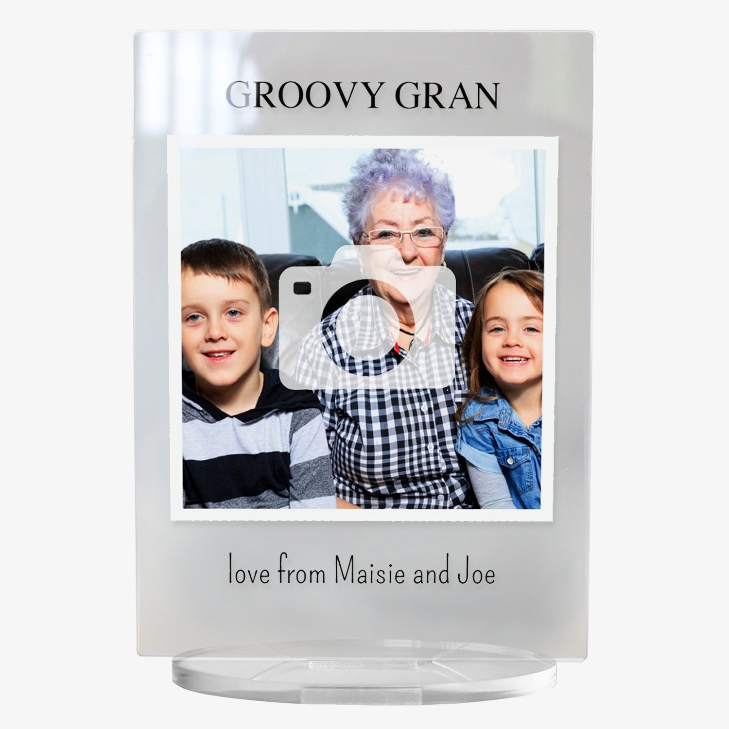 A personalised photo plaque with a clear acrylic frame. The top text reads 'GROOVY GRAN' in capital letters. The central section features a photo of an elderly woman with short purple hair sitting between a smiling boy and girl. Below the photo, the text reads 'love from Maisie and Joe'. The plaque stands on a clear oval base.