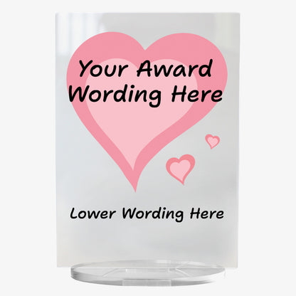 A clear acrylic award plaque standing on a circular base, featuring a large deep pink heart with pale pink centre,  with 2 smaller hearts at its tip . Overlaying the heart is placeholder text reading 'Your Award Wording Here' in bold black font. Below, additional text reads 'Lower Wording Here'. 